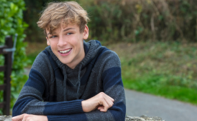 Success stories - young man smiling with countryside and lane behind him